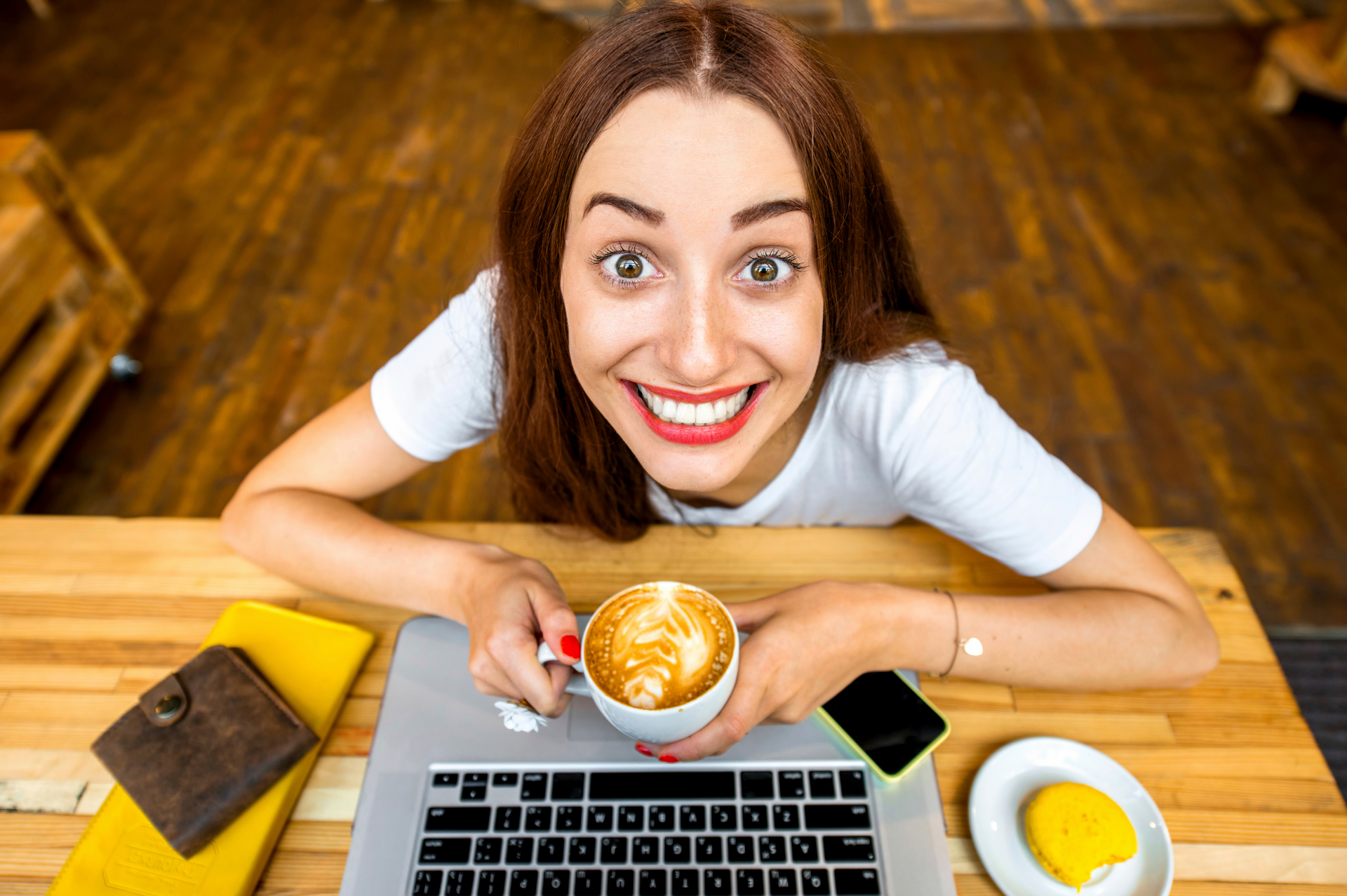 Young woman enjoying cappuccino sitting with laptop in the wooden cafe interior. Top view